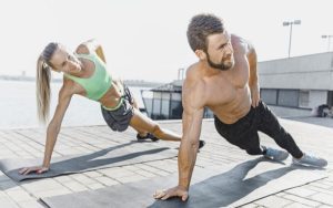 Lean man and woman doing side planks outside